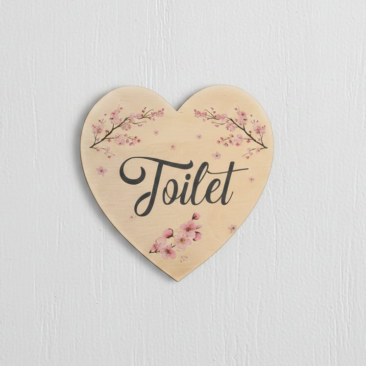 Heart-shaped wooden toilet sign with pink cherry blossom branches and the word 'Toilet' in black script, shown on a white background.