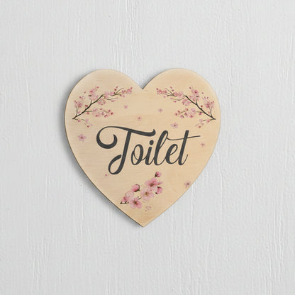 Heart-shaped wooden toilet sign with pink cherry blossom branches and the word 'Toilet' in black script, shown on a white background.