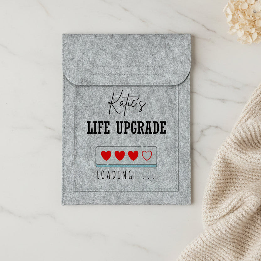 A personalized gray felt laptop sleeve with a flap, featuring the text 'Katie's LIFE UPGRADE' and a 'LOADING .