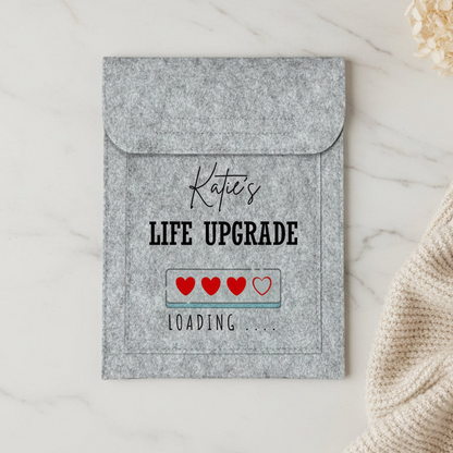 A personalized gray felt laptop sleeve with a flap, featuring the text 'Katie's LIFE UPGRADE' and a 'LOADING .