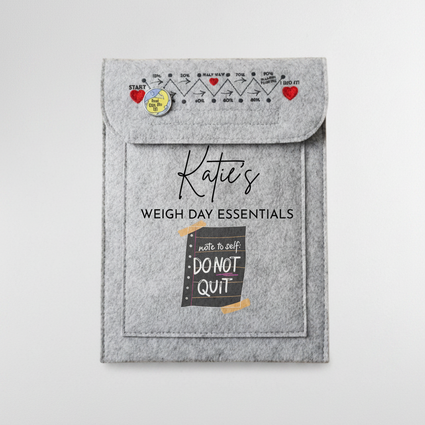 A gray felt pouch labeled 'Katie's WEIGH DAY ESSENTIALS' with a flap closure, printed weight-chart graphics, and a pocket reading 'write to self DO NOT QUIT', shown on a white desk with a keyboard corner and binder clip nearby.